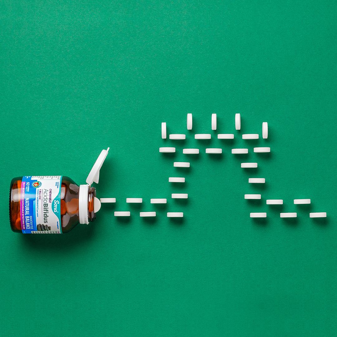 Opened bottle of Sona AcidoBifidus Chewable Probiotics with tablets arranged artistically on a green background. Each tablet contains 16 billion probiotics, promoting a healthy immune system and digestive balance. Vegan, natural citrus flavor